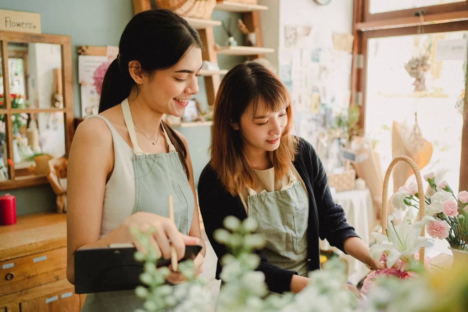 Two florists in aprons smiling as they arrange flowers in their shop