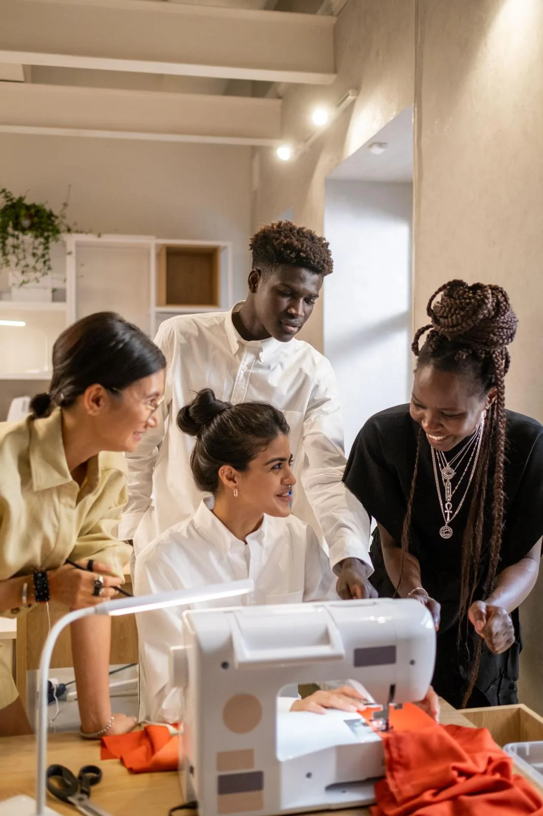 A group gathered around a sewing machine, smiling as they work on a garment together