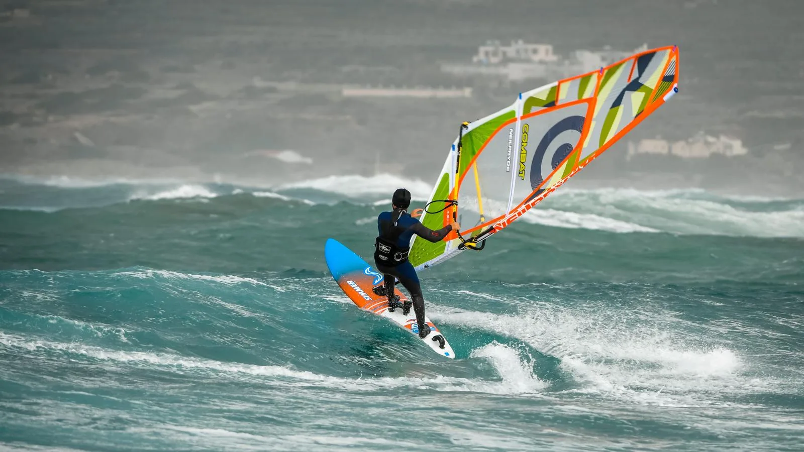 A windsurfer riding a wave on a bright, blustery day
