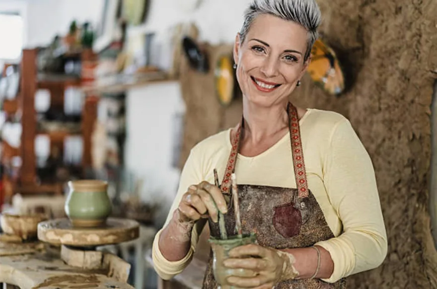 A smiling woman shaping a pot in a pottery studio